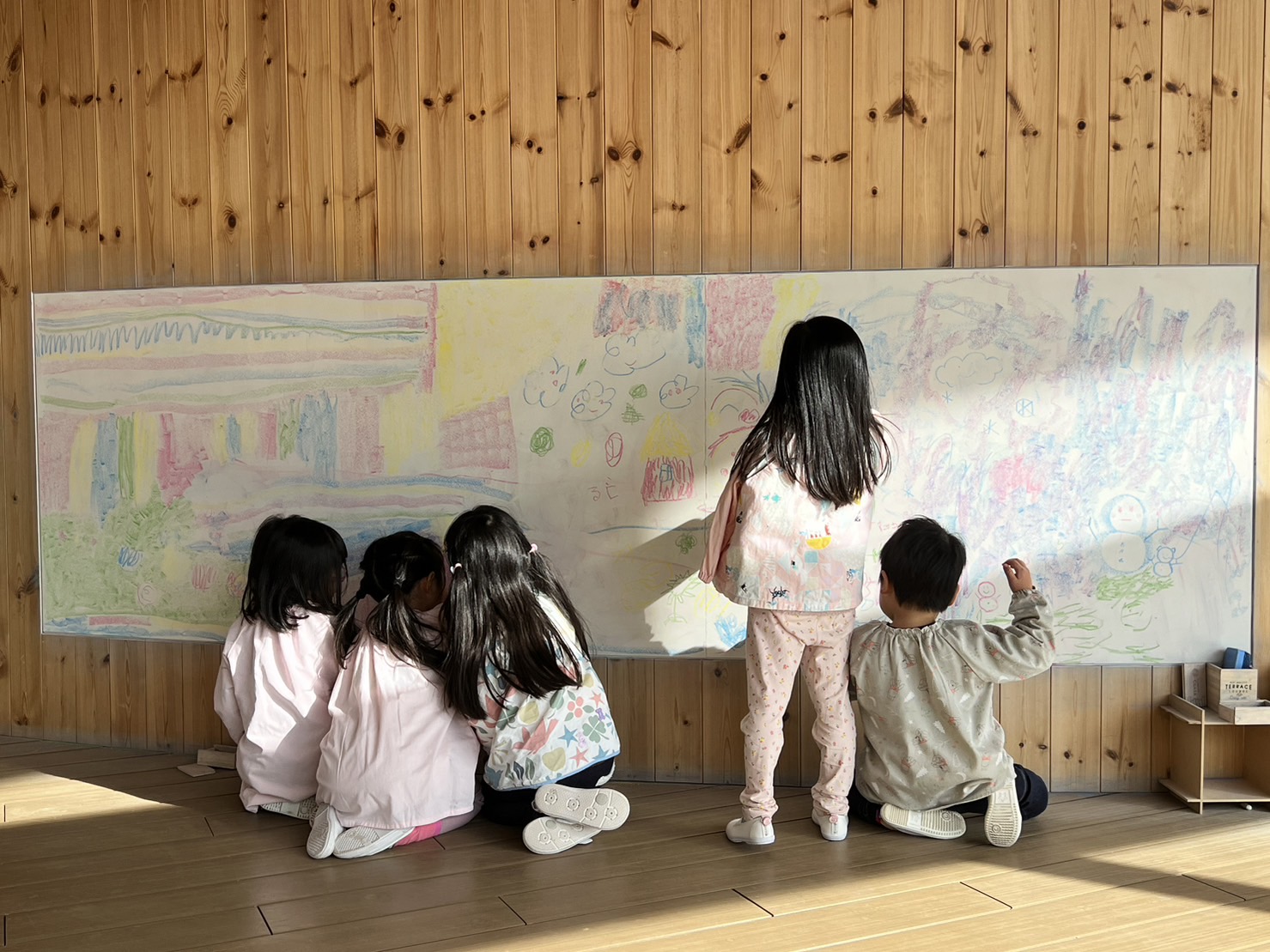 白い黒板に子どもたちがカラフルに絵を描いている
